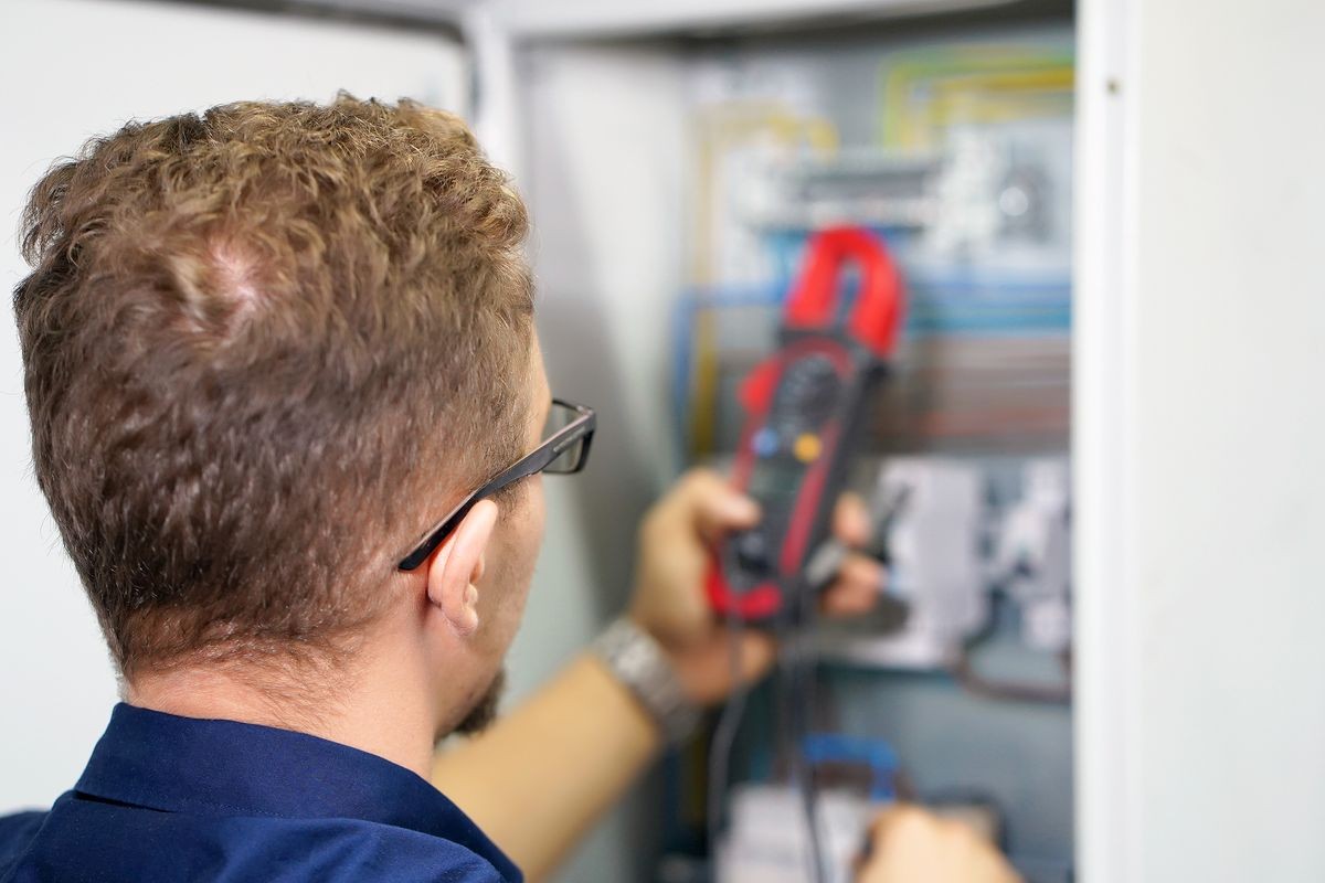 Close-up electrician measures voltage with multimeter in electrical cabinet. An electrician is checking the voltage in an electric box.